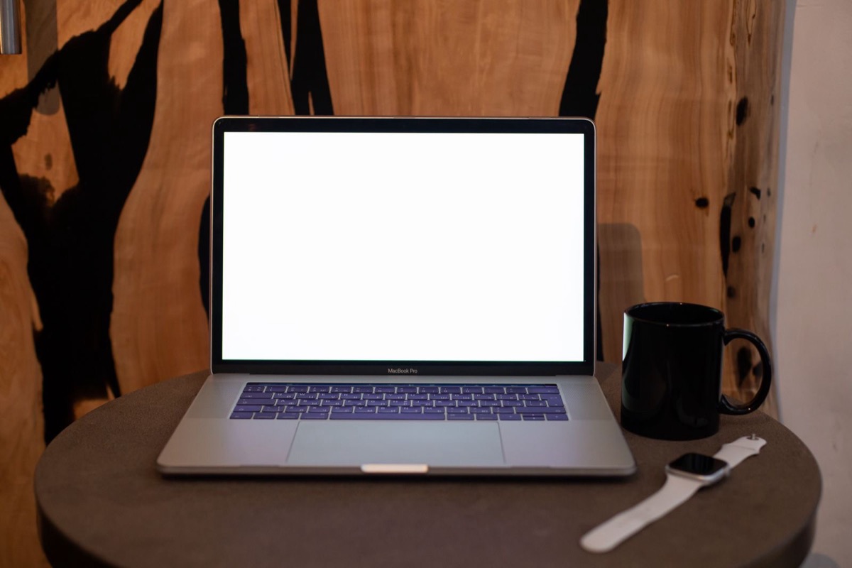 A laptop with a blank screen and a mug on a round table