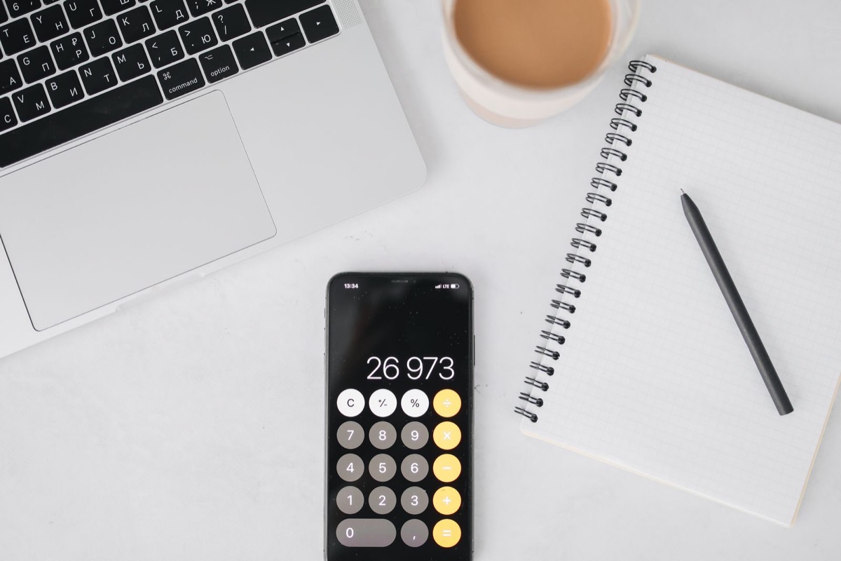 A laptop, a phone calculator and a notebook on a white desk