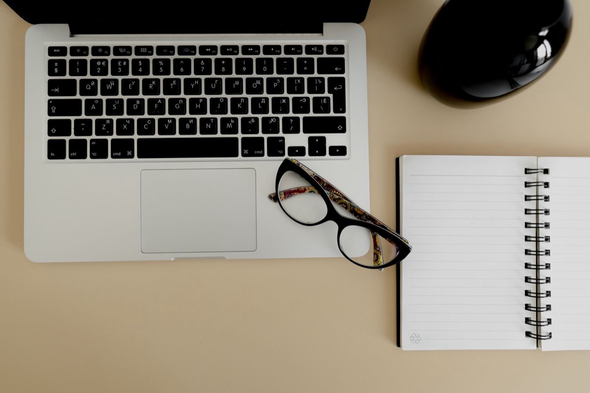 A laptop, glasses and a notebook on a desk